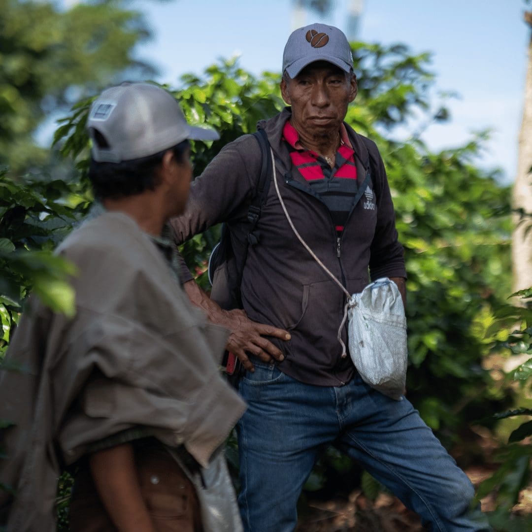 Two men standing outdoors with greenery in the background